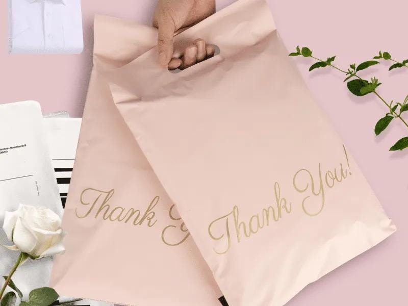 Beige-colored poly bags with "Thank You" inscribed on them, surrounded by leaves and other items, placed against a pink background, creating a warm and nature-inspired design.