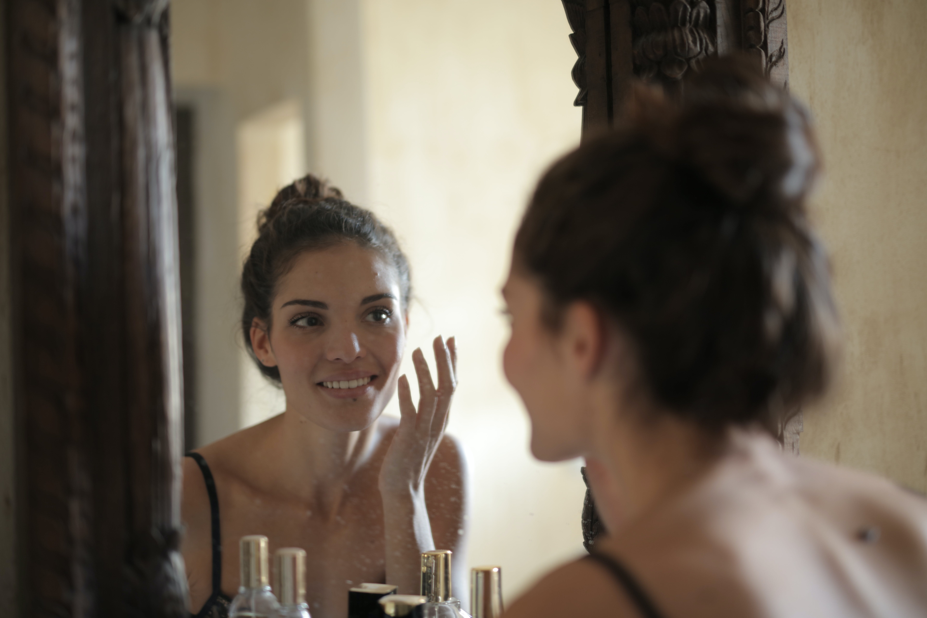 Woman standing at mirror, applying kumkumadi oil. skin care routine, self care, self love.
