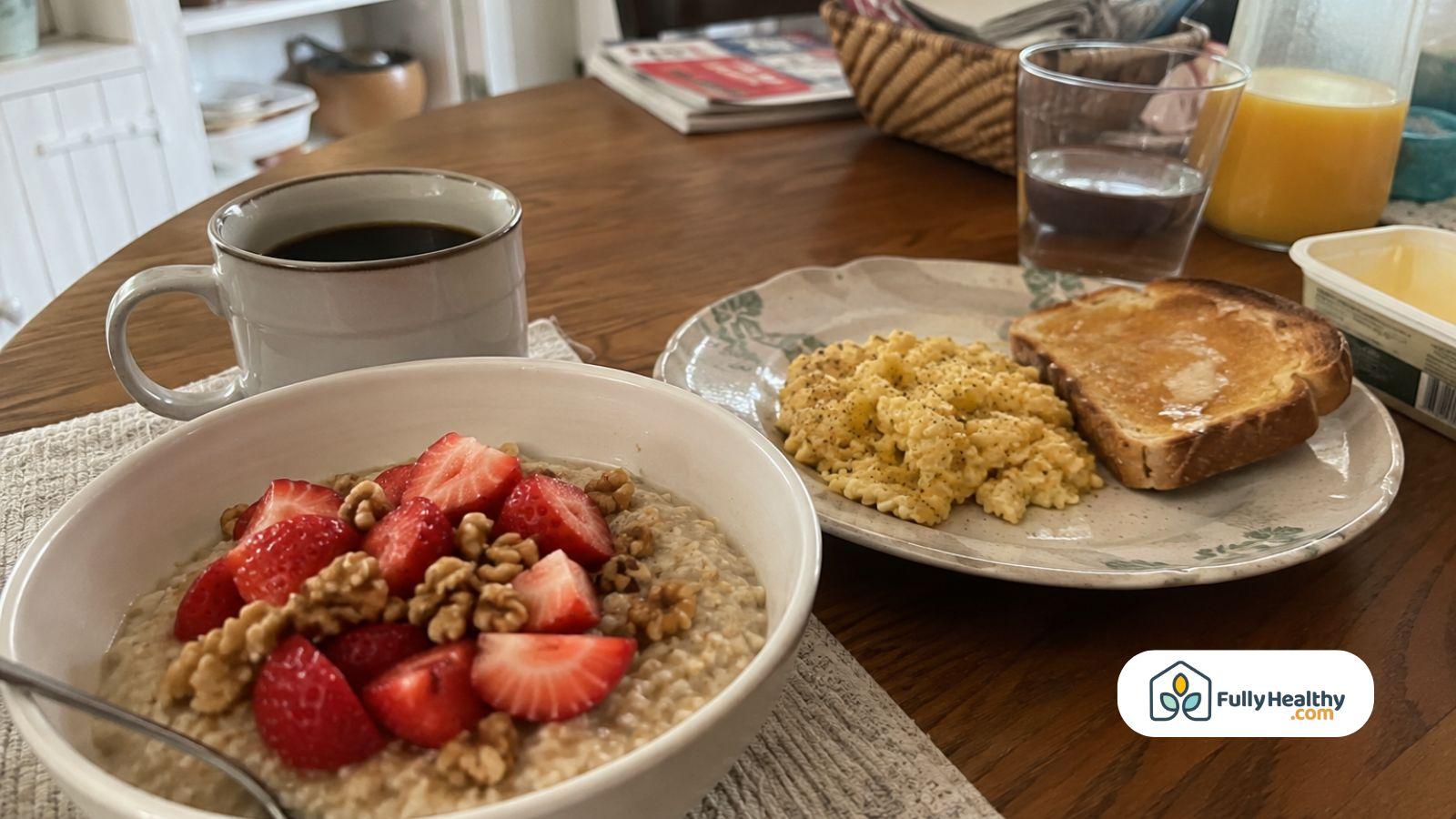Bowl of oatmeal topped with strawberries and walnuts served beside scrambled eggs and a toast.