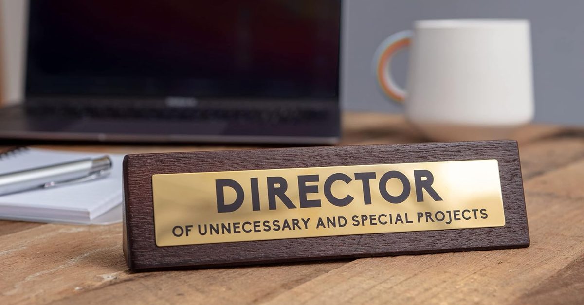 Een hout bordje met een goud gedeelte waarop staat "Directeur van onnodige en speciale projecten".