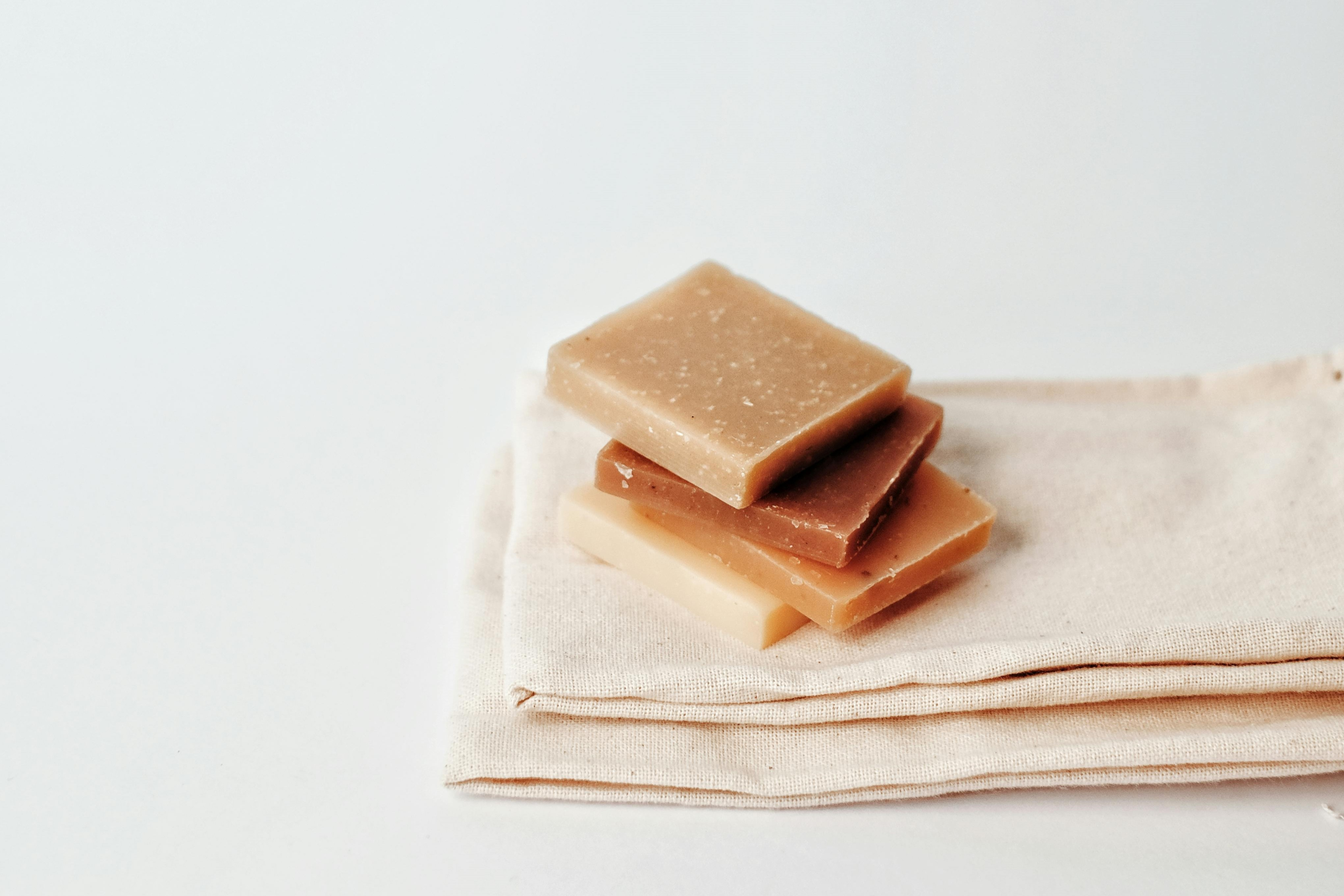 A minimalistic setup featuring four soap pieces stacked atop a folded cloth, against a white background.