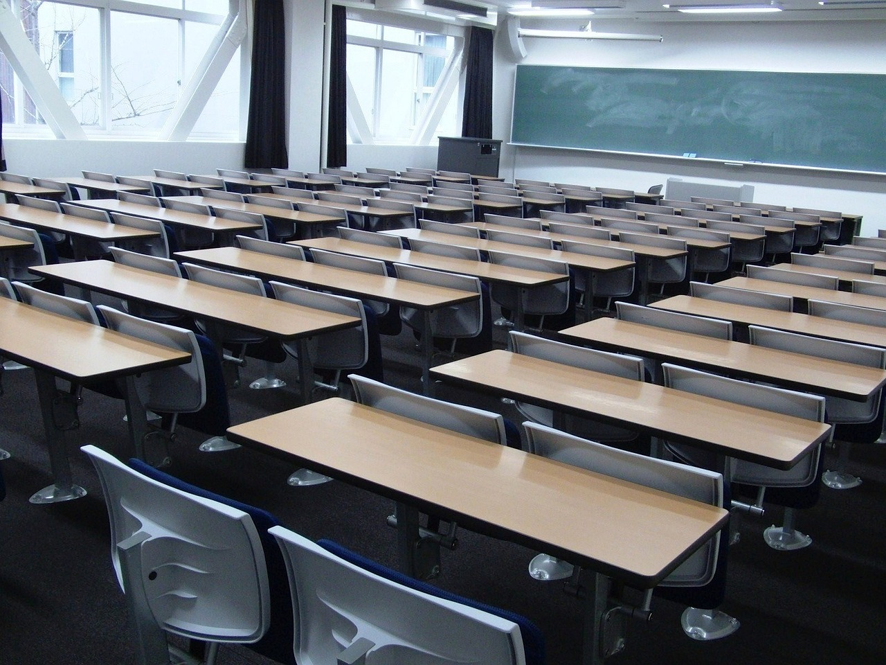 A university classroom with a blackboard and neatly arranged chairs and desks. 