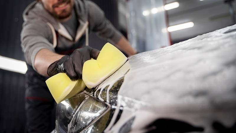 scrubbing the car hood with a yellow sponge