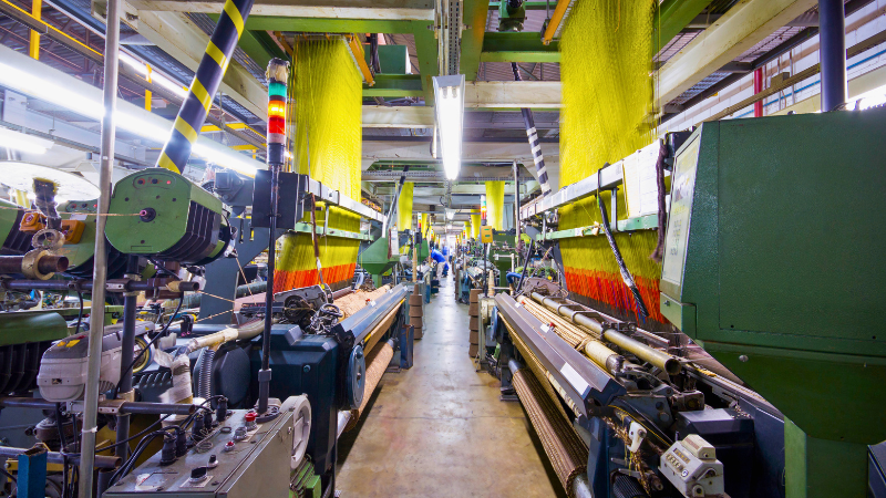 A view down a factory aisle lined with automated looms, with yellow and red threads visible on the machines.