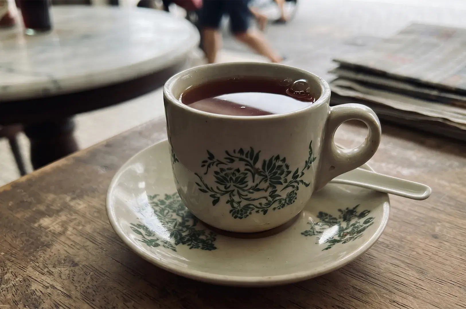 Traditional floral kopitiam ceramic cup filled with hot tea on a wooden table.