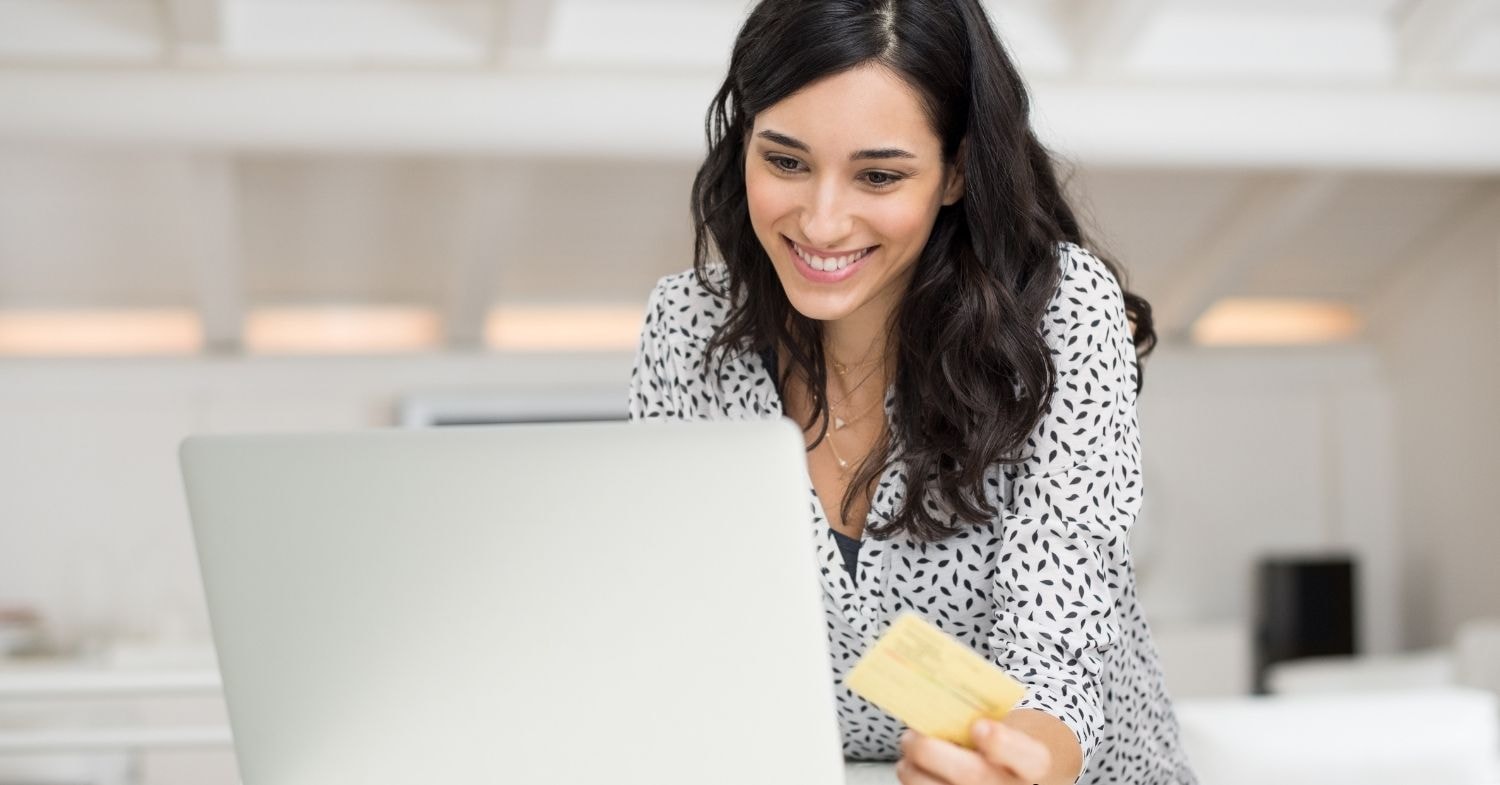 Woman smiling while using her laptop to pay excise tax online with a credit card.