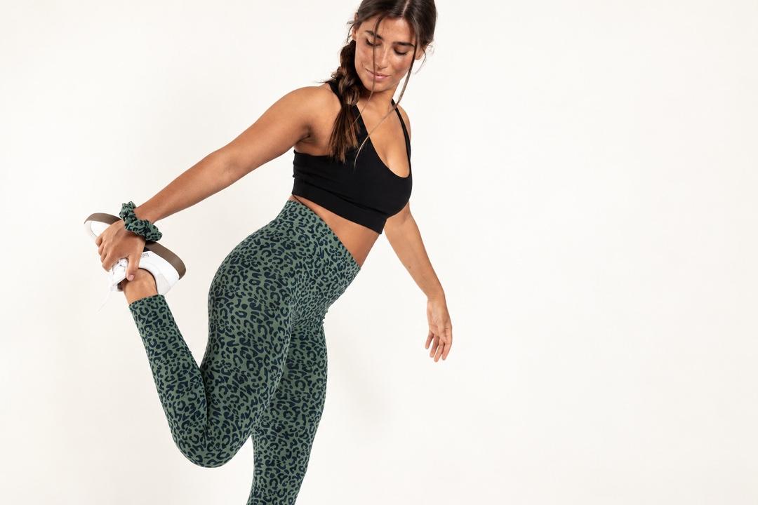 Frau beim Dehnen in olivfarbenen Orbasics-Leggings mit Leopardenmuster und schwarzem Sport-BH.