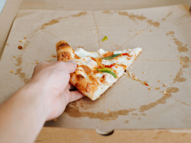 hand grabbing the last slice of pizza from a grease stained pizza box