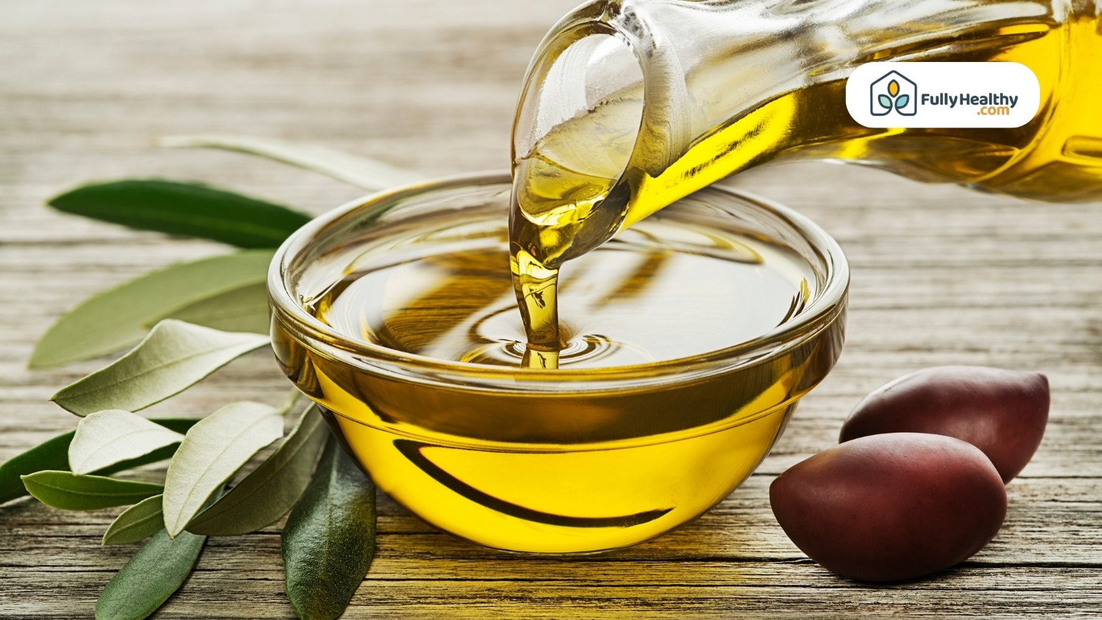 Golden olive oil poured into bowl with leaves and dark olives