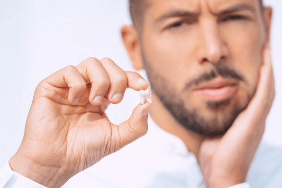 man holding extracted tooth biting on gauze pad