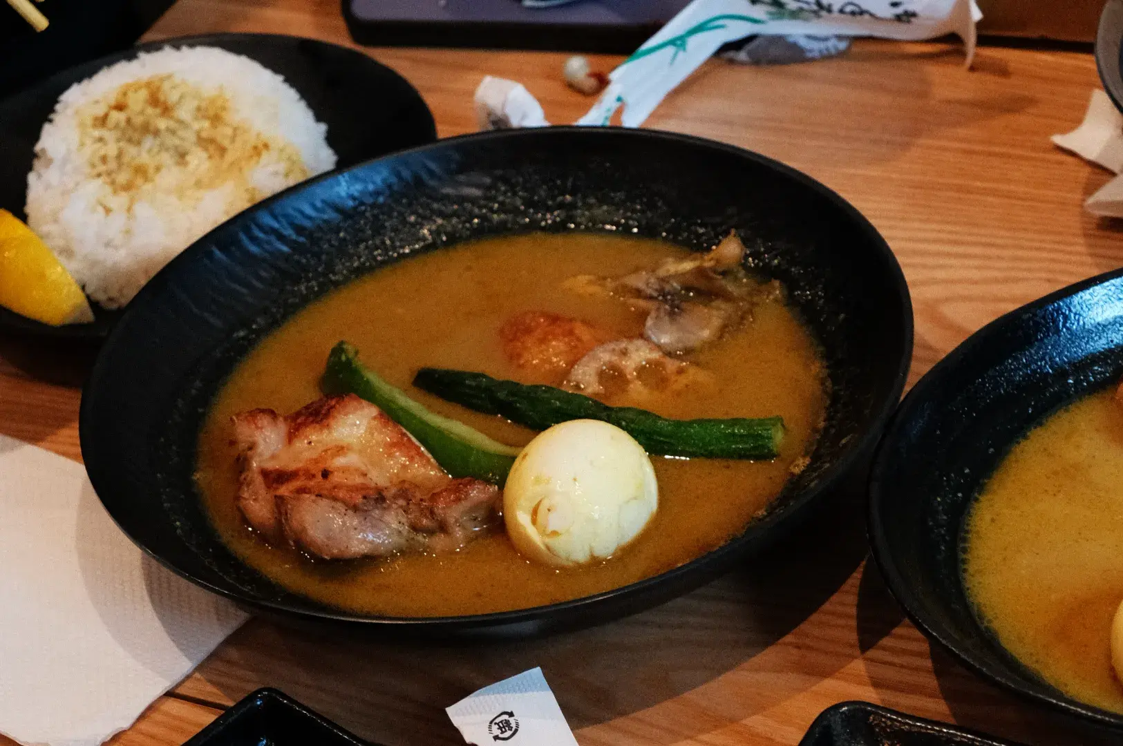 A bowl of ramen soup with chicken, boiled egg, and green vegetables, accompanied by a side of rice.