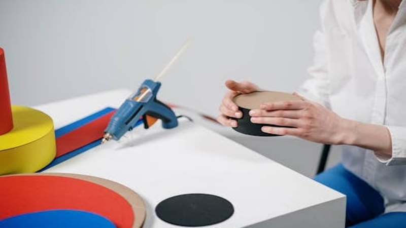 Woman using a hot glue gun for colorful craft project with foam circles on a white table