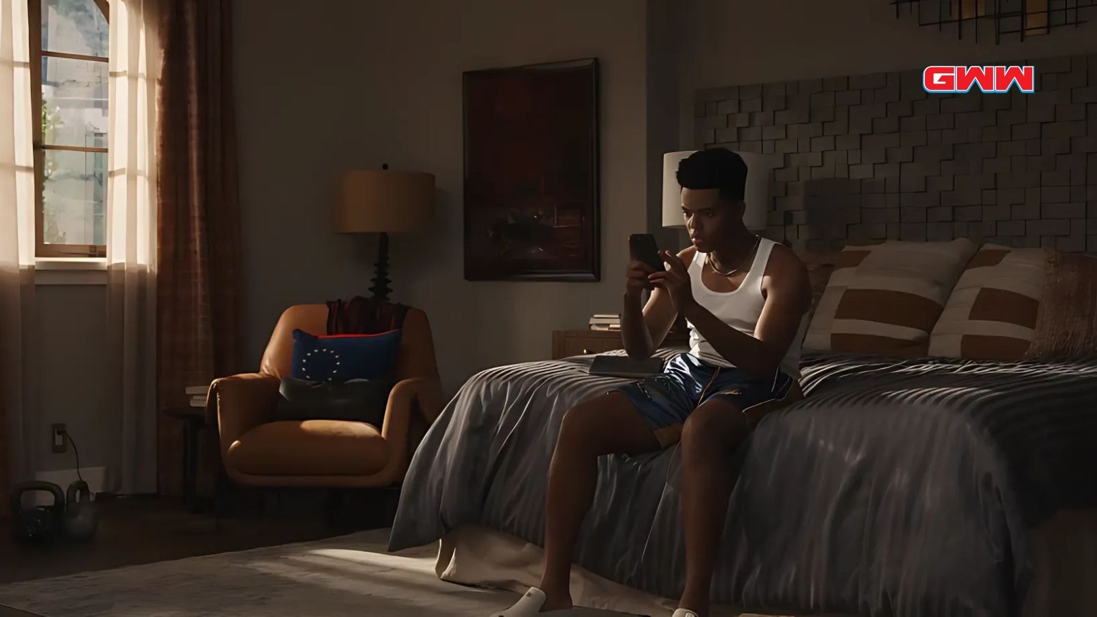 Jabari Banks sitting on bed looking at phone in bedroom scene