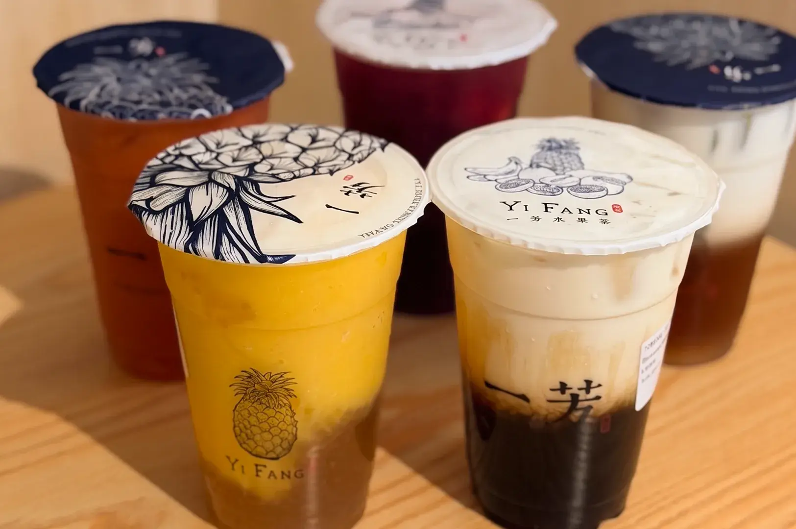 Group of five sealed Yi Fang Taiwan Fruit Tea cups with various colorful tea and milk tea layers on a wooden table.
