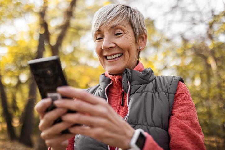 Happy mature woman in a brown vest sending a text message while out for a walk.