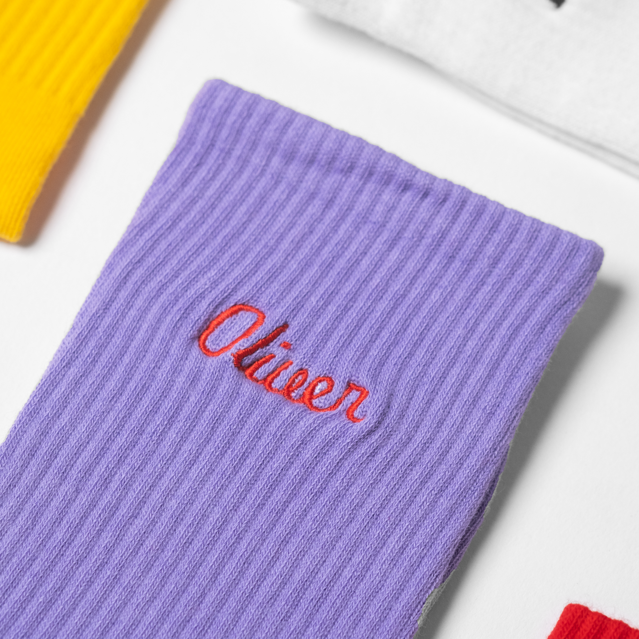A flat-lay image of custom mens purple crew socks with the male name 'Oliver' embroidered in red thread.