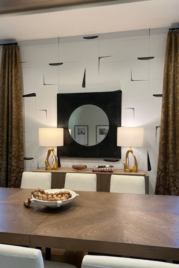 Contemporary dining room with graphic wallpaper, circular mirror, gold lamps, and wood sideboard.