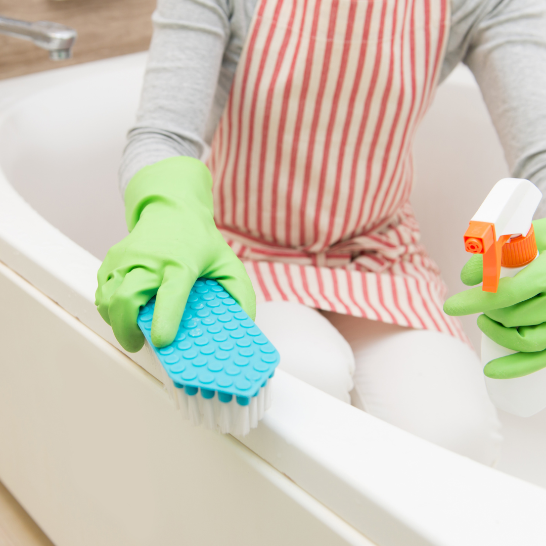person cleaning their bathtub with a spray bottle and scrubbing brush