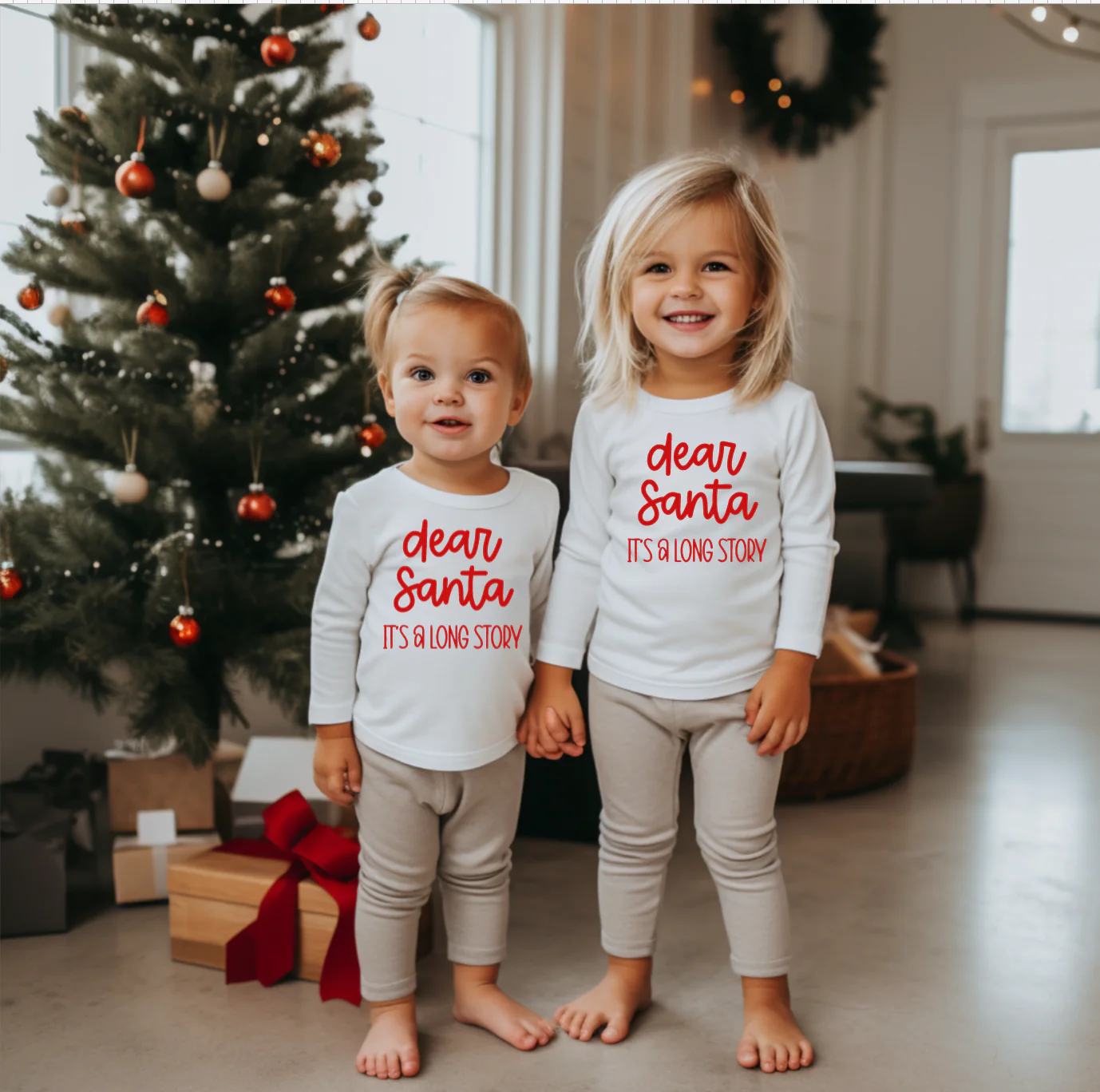 a little girl and her big sis wearing matching Dear Santa matching tees next to a Christmas tree