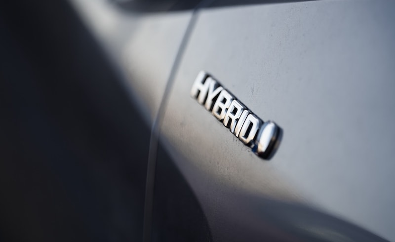 Close-up of a Toyota hybrid badge on a sleek silver vehicle, showcasing fuel efficiency and eco-friendly technology at AutoFair Toyota of Tewksbury in Tewksbury, MA