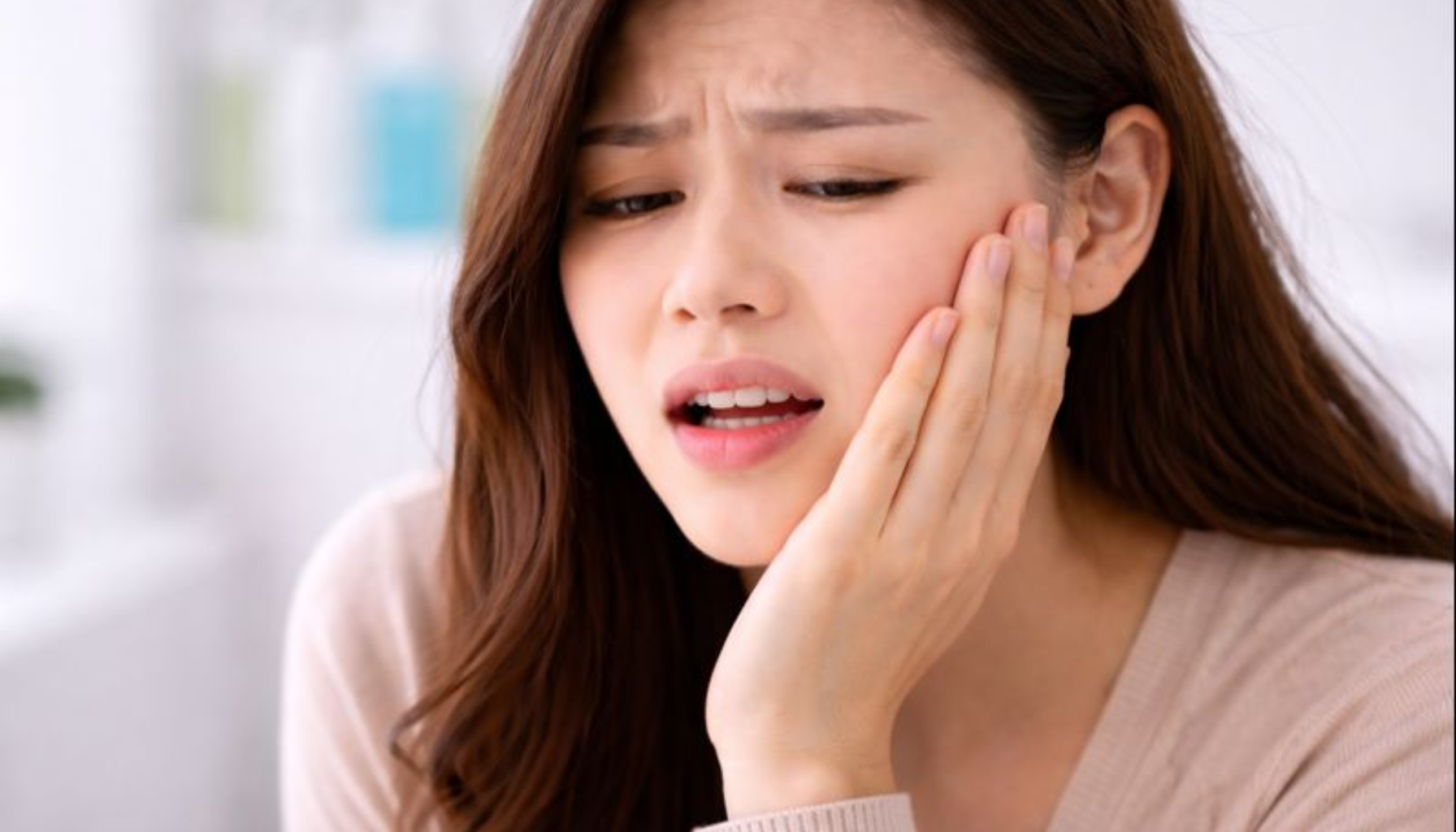 Tannsmerter: Når Smerten Forteller at Noe er Galt 13 Kvinne holder seg til kinnet og viser tydelig tannverk, med smertefullt uttrykk i rolig bakgrunn.