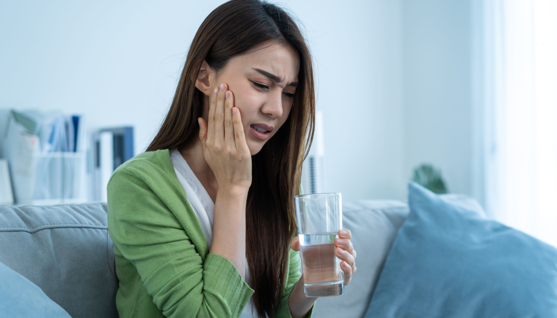 Ising i tennene etter fylling – Hva er normalt? 2 Kvinne med smertefullt uttrykk holder seg til kinnet og et glass vann, muligens på grunn av tannfølsomhet eller tannverk.