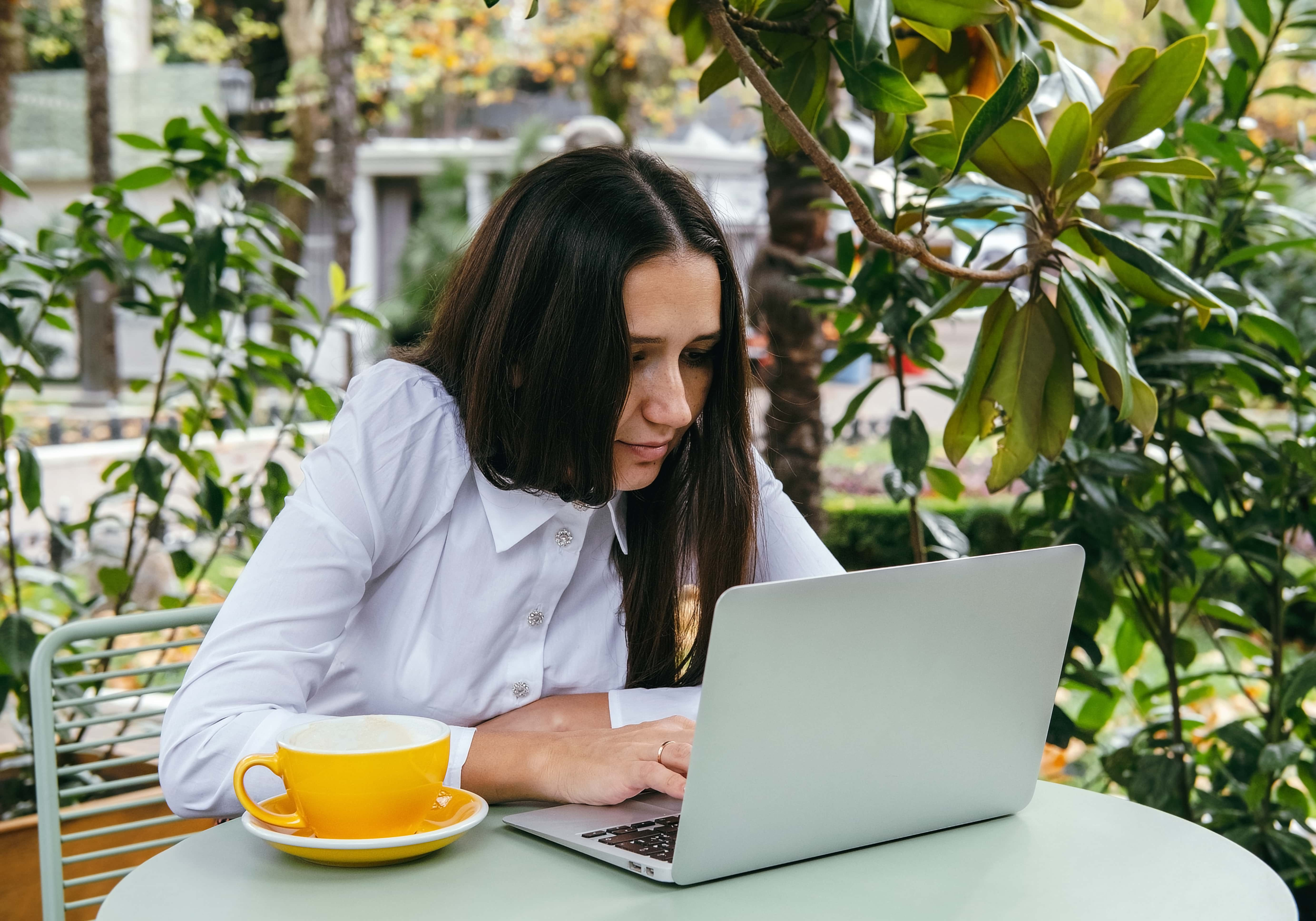 woman sitting with bad posture on laptop.  She has a yellow cup of coffee next to her.  There is a tree in the background. Strathfield chiro or Five Dock chiro treatment to relieve pain.