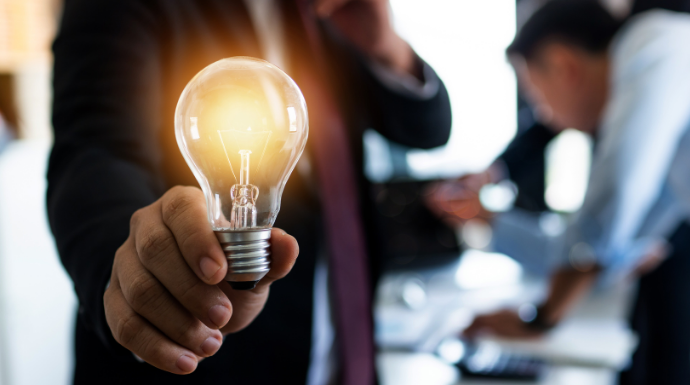 Visual example of innovation, a team member holding a lightbulb. Innovating manufacturing companies may include ideas that revolve around digital manufacturing, creating a smart factory, and improving data visibility to make informed decisions. 