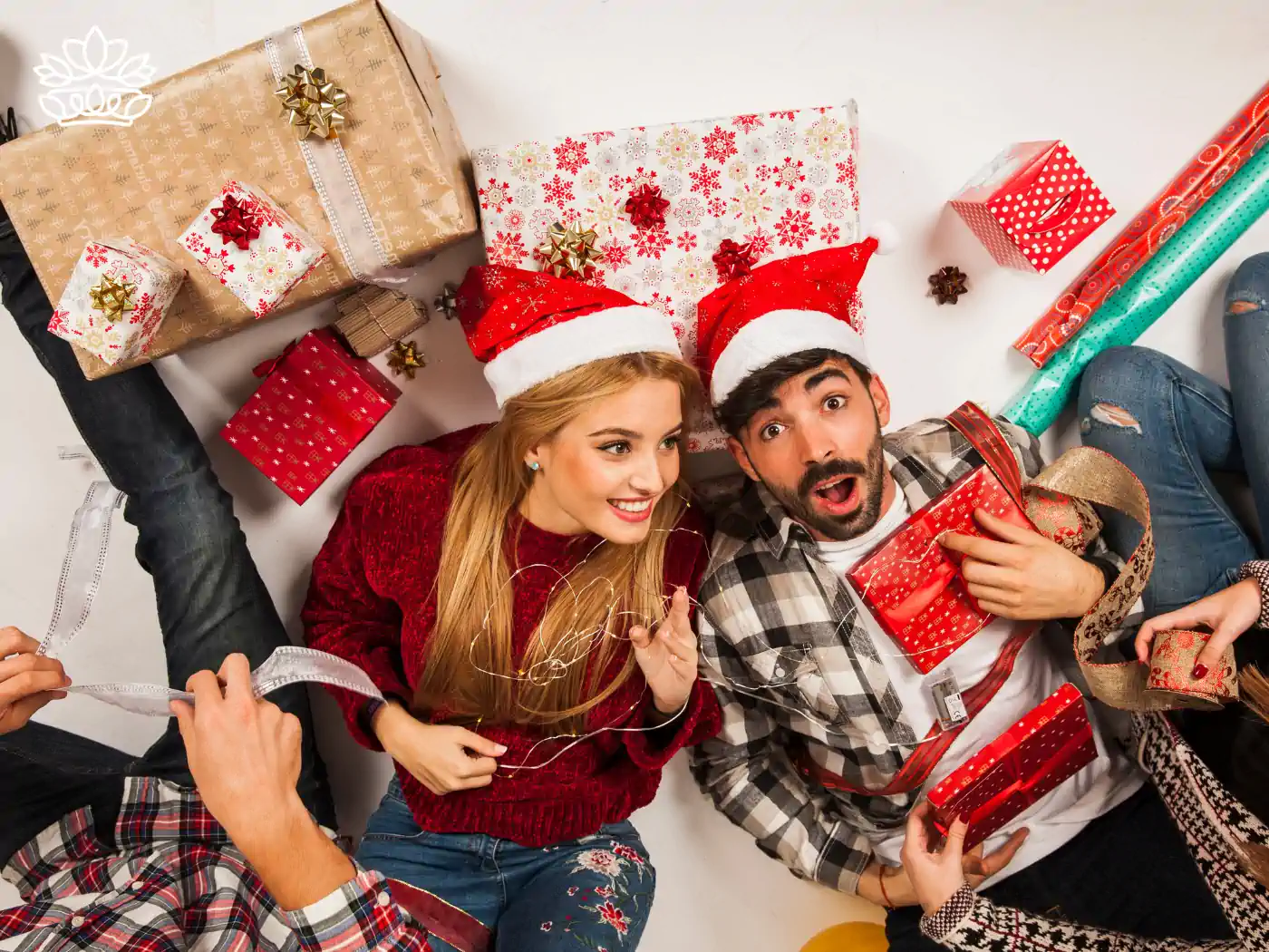 A group of friends wrapping gifts together on the floor, surrounded by brightly colored gift boxes, wrapping paper, and ribbons, part of the Festive Season Gift Boxes Collection. Delivered with Heart by Fabulous Flowers and Gifts.