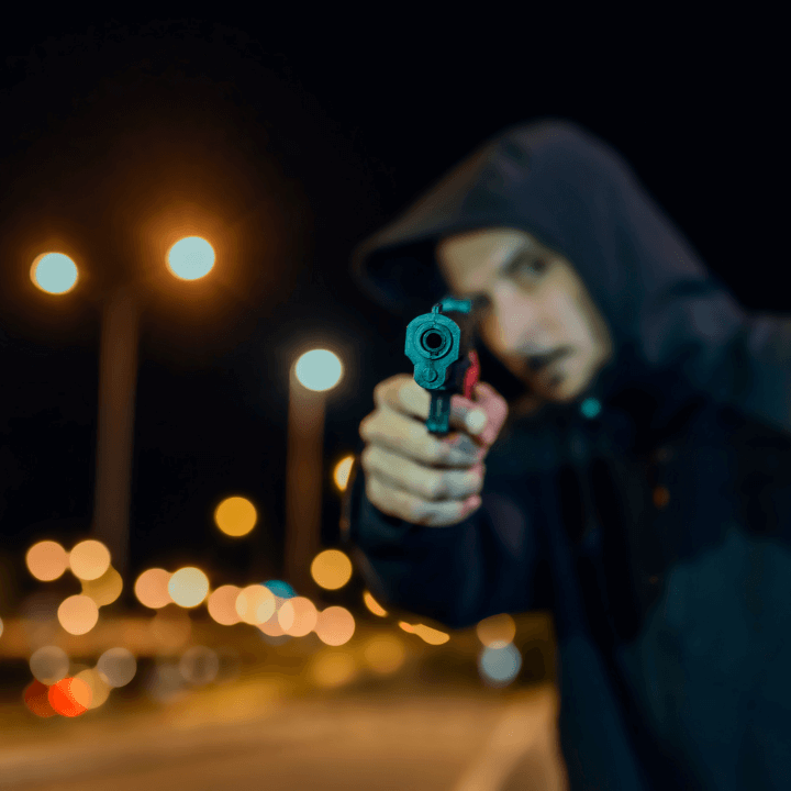 a man with his hood up pointing a handgun at the camera