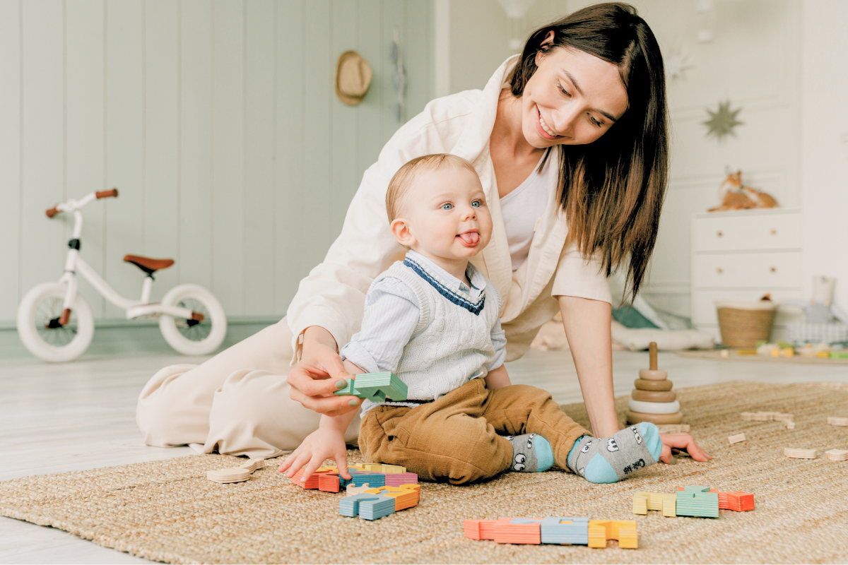 Baby boy sitting up next to mom while playing with toys. Poppyseed Play