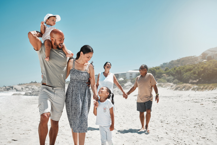 Happy young family of four and grandparents walking on the beach.