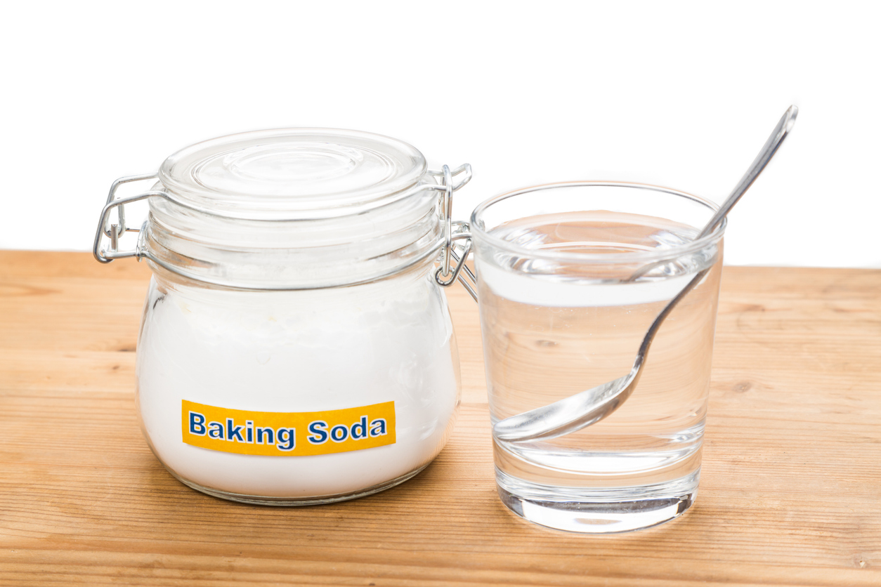 An image of a jar of baking soda and a glass of water with spoon on a wooden table. 