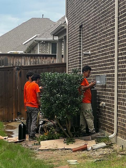 The image shows an HVAC Services Pro installation team, consisting of technicians in navy shirts, completing the startup and testing of a new HVAC system. They are focused on ensuring the system operates efficiently, which will help in reducing energy bills and improving overall energy efficiency for the home.