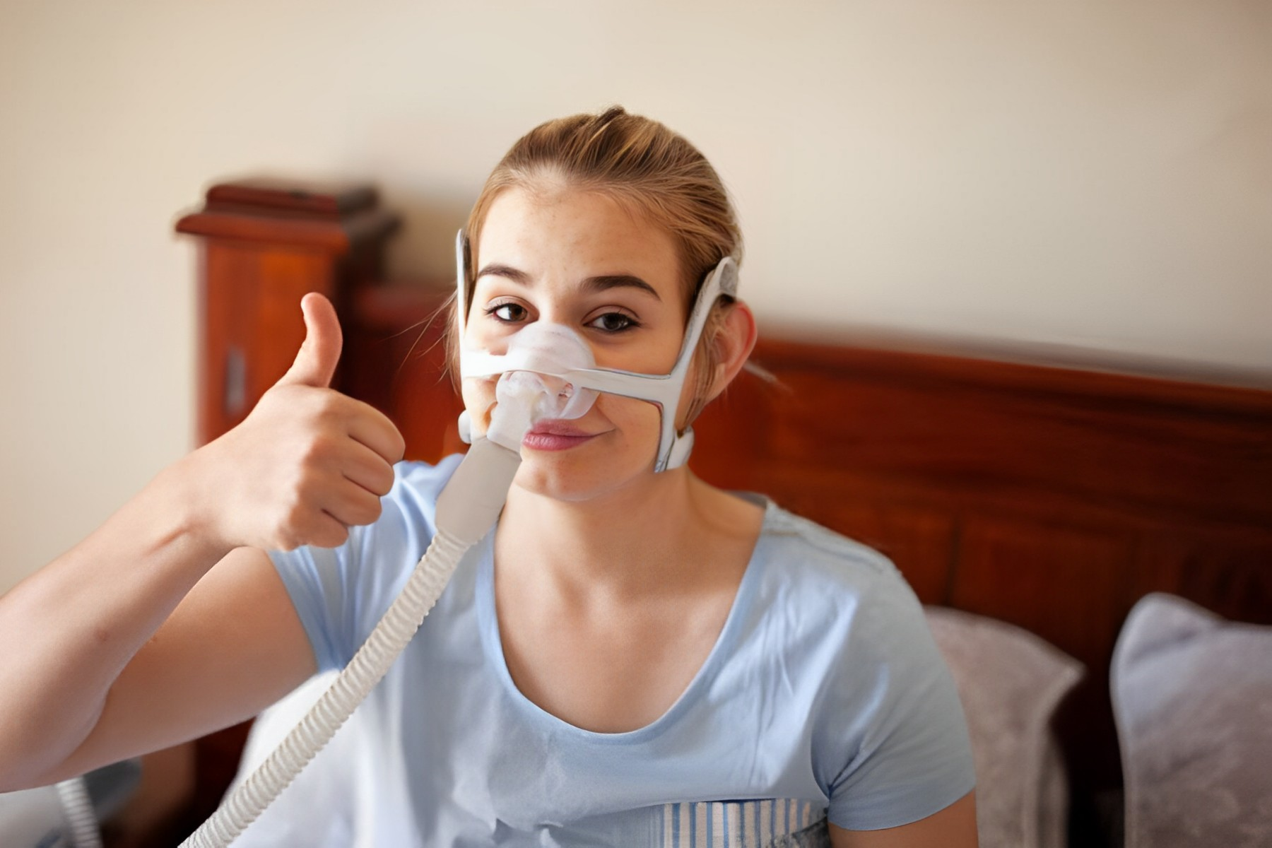 A photo of a teenage girl having a thumbs-up while using CPAP