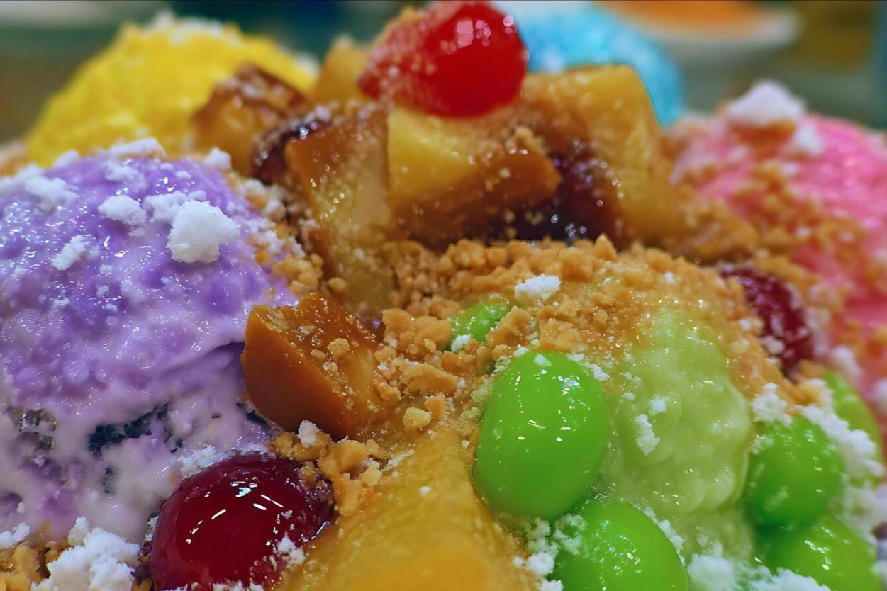 This extreme close-up shot focuses on a colorful, layered dessert, most likely Halo-Halo, featuring a scoop of bright purple ice cream (ube) and scoops of yellow, pink, and blue components.