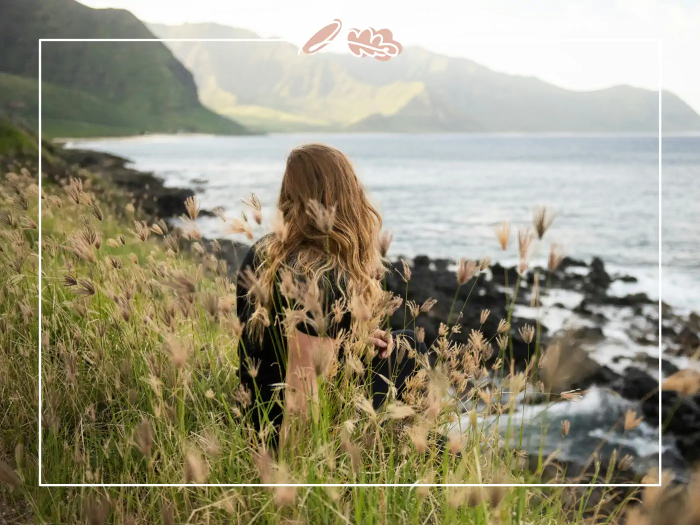 A woman with long hair sitting in tall grass by the sea, reflecting on nature's peace and tranquillity during a busy day.