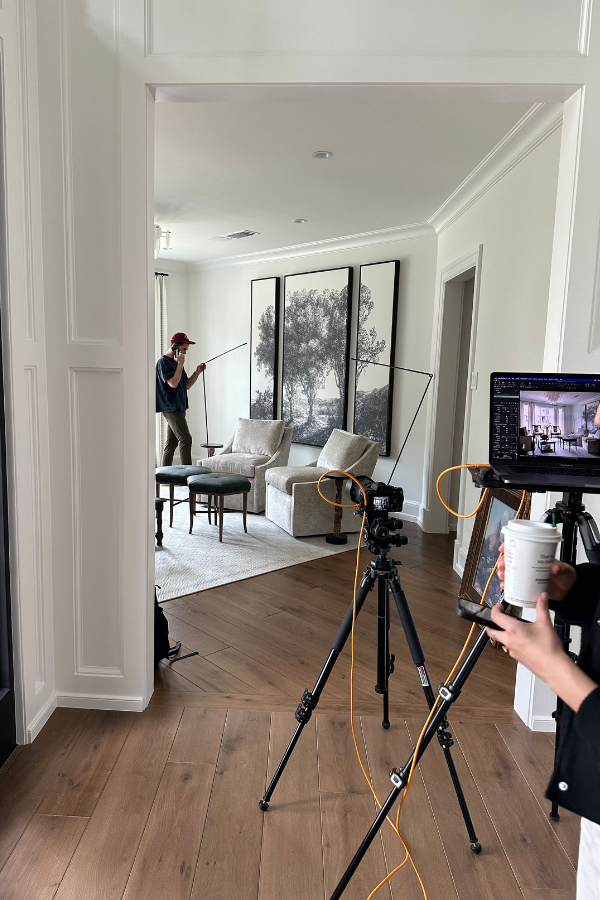 a woman takes photos of a living space with three paintings while a man adjusts lighting