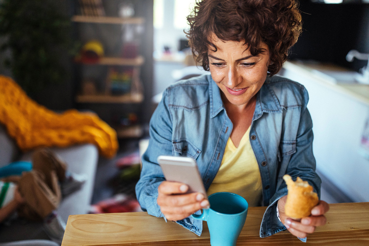 Woman in a blue shirt having coffee and checking her phone. 