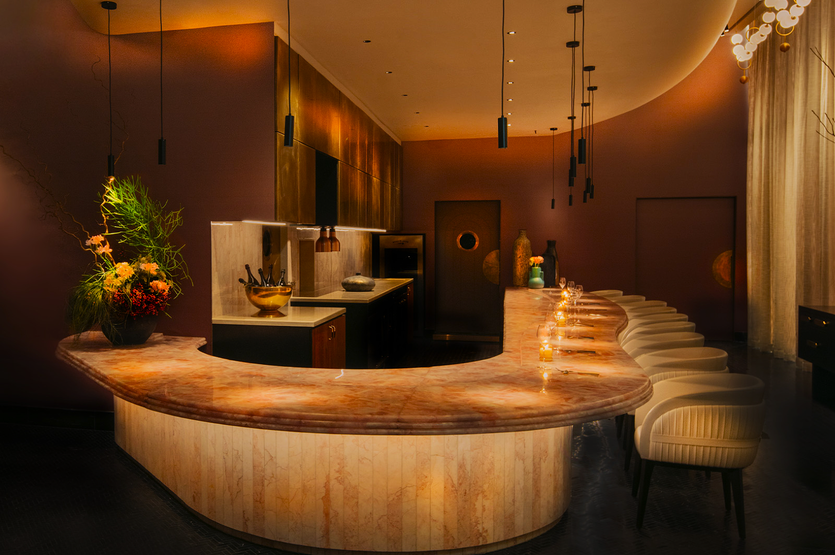 Elegant bar interior with a curved marble counter, soft lighting, and padded chairs. A modern, inviting ambiance with a touch of luxury and warmth.