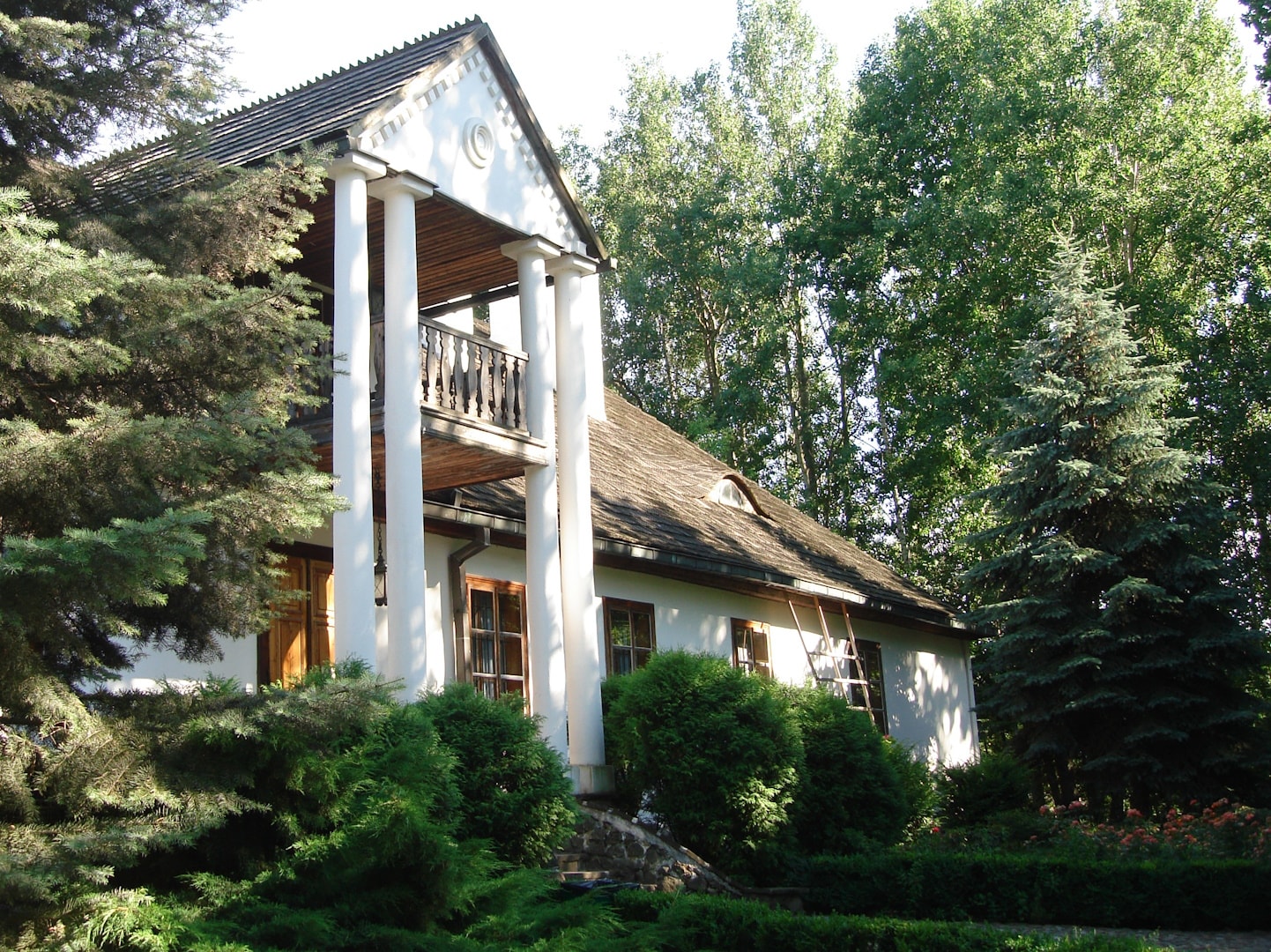 Muzeum Wsi Radomskiej i imponująca zabudowa, jaką jest biały dom pośrodku drzew z wysoką kolumnadą. Źródło: https://commons.wikimedia.org/wiki/File:Muzeum_Wsi_Radomskiej_%2823%29.jpg