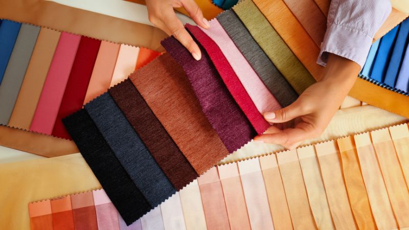 A person is holding a piece of fabric in front of a variety of colors