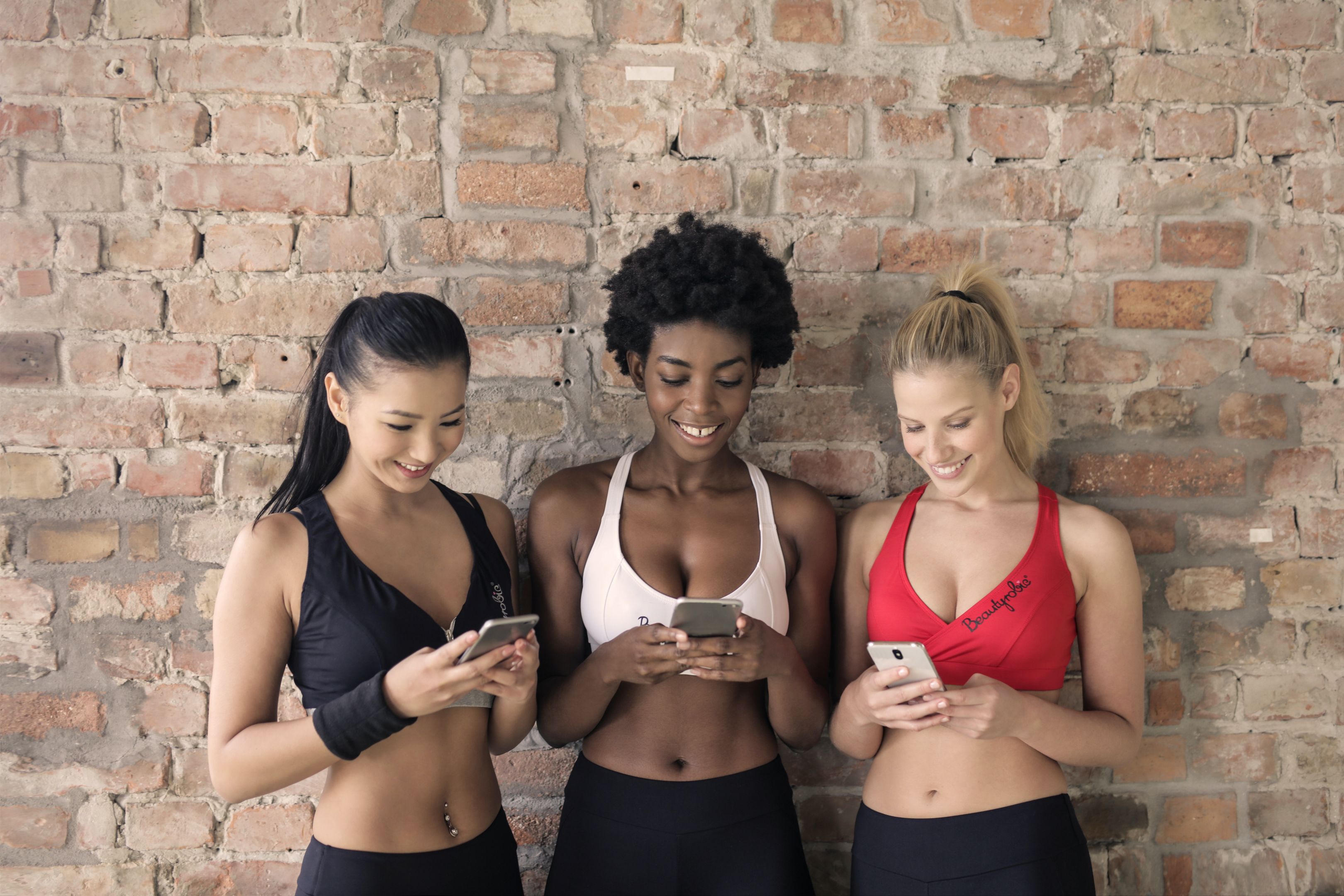 Das Bild zeigt eine Gruppe von drei Frauen, die auf ihre Handy gucken, nachdem sie sich für unseren Newsletter angemeldet und die Vorteile unserer Infos bemerkt haben. 