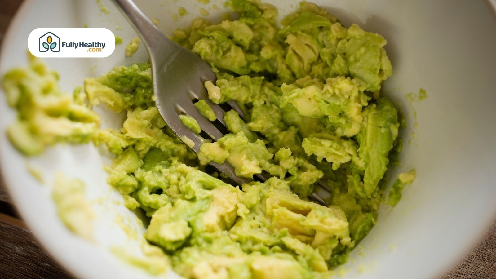 Mashed avocado in white bowl with silver fork