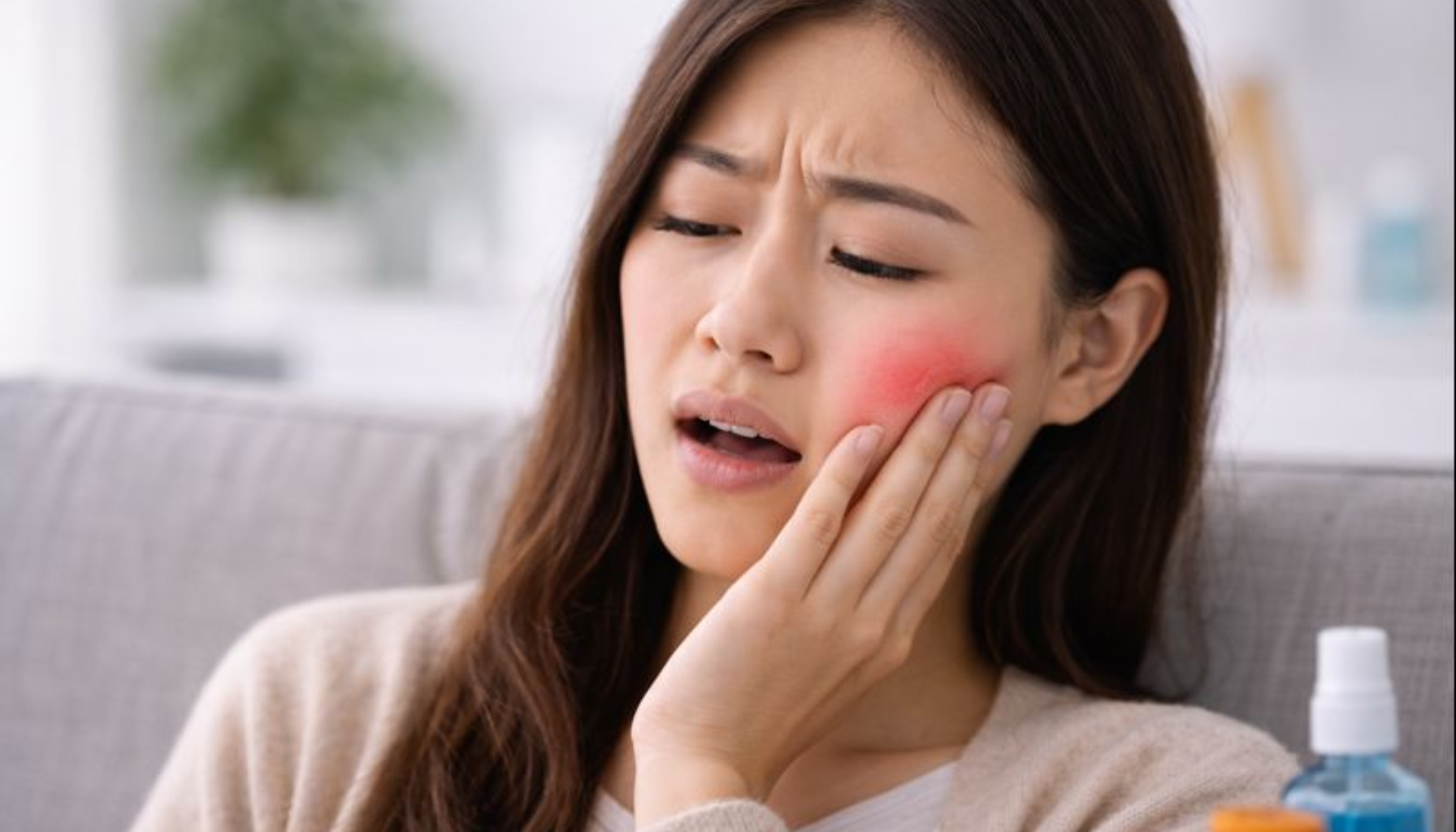 Betennelse Etter Trekking av Tann: Når Helingen Går Galt 11 Kvinne med betent kinn etter tanntrekking holder hånden mot smerten, omgitt av medisiner hjemme.