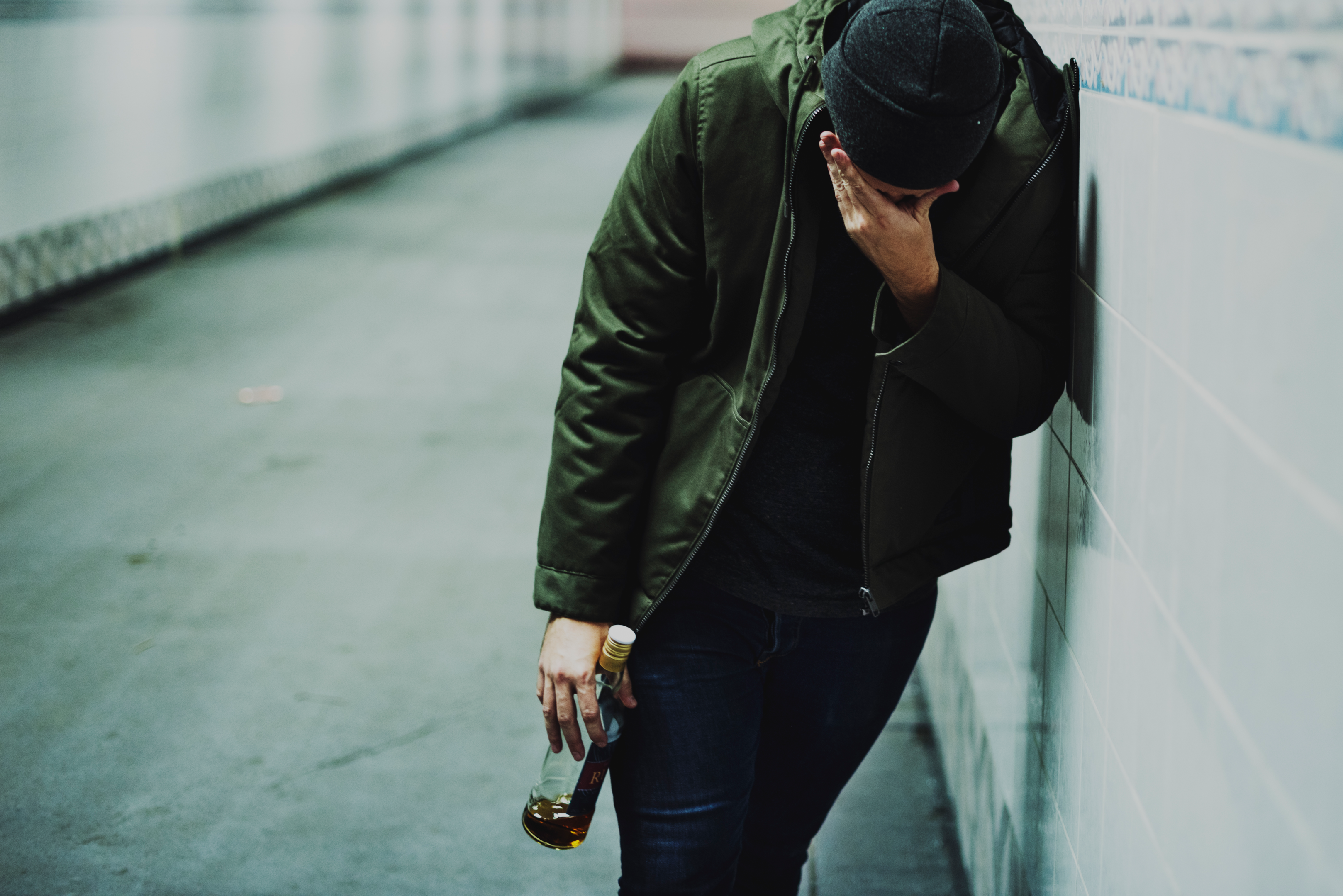Man grappling with homelessness and addiction, clutching a liquor bottle.