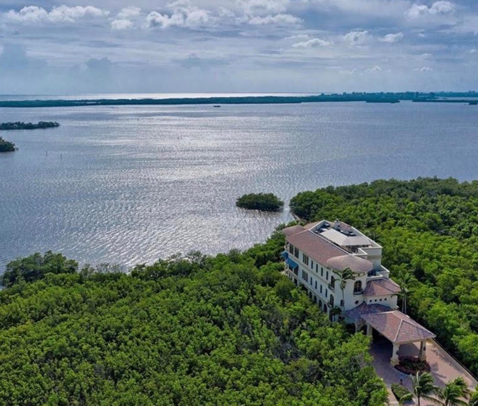 The image depicts a golf course clubhouse designed in Mediterranean architecture, surrounded by lush palm trees, embodying the essence of elevated coastal living. This inviting space is part of the exclusive Colony at Pelican Landing, offering world-class amenities and a picturesque setting for both relaxation and recreation.