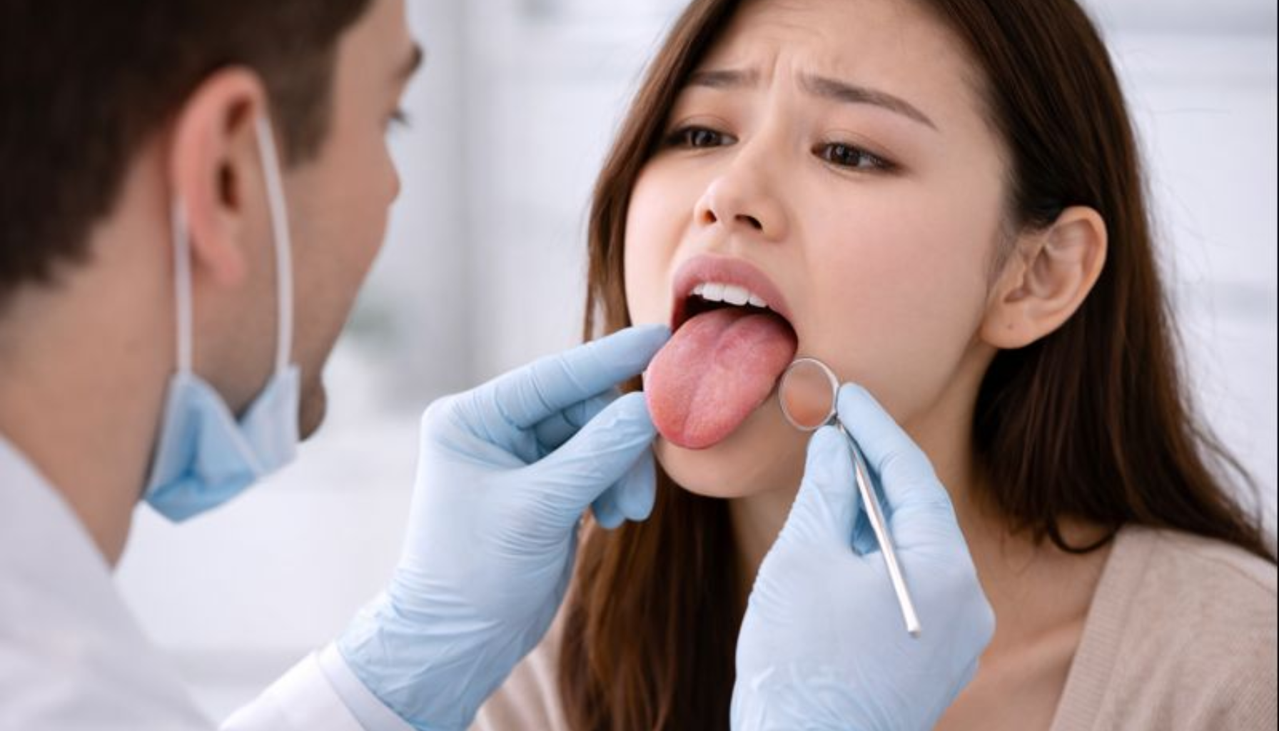 Hoven Tunge: Når Hevelse Gjør Det Ubehagelig å Snakke og Spise 14 Tannlege undersøker kvinnens tunge med speil, mens hun sitter i tannlegestolen og viser ubehagelig hevelse.