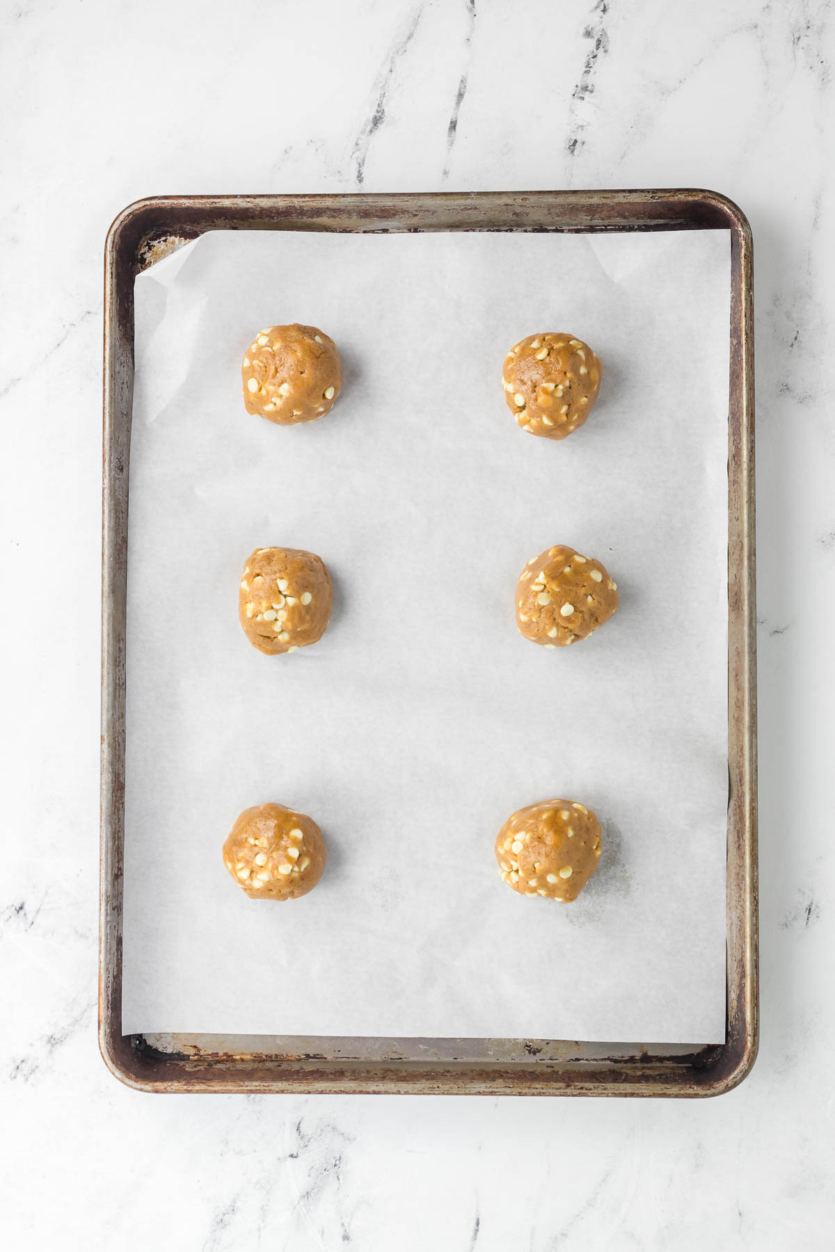 six biscoff dough balls on a baking sheet with parchment paper