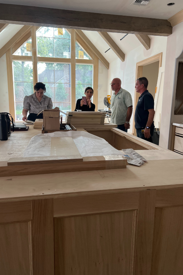 Kitchen renovation in progress with installed stone backsplash, unfinished cabinetry, and architectural millwork detailing.
